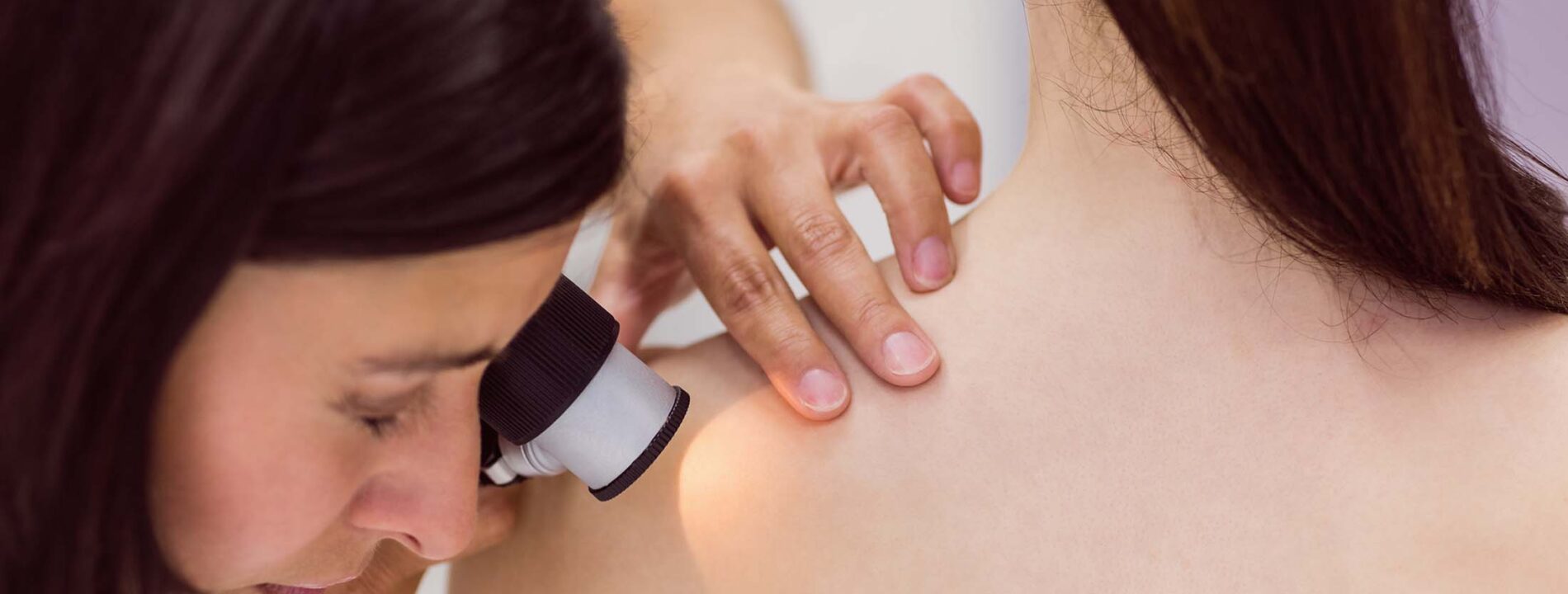 Dermatologist examining skin of patient with dermatoscope in clinic